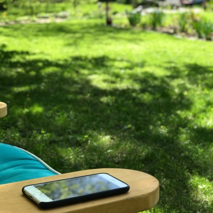 An iPhone sitting on the arm of a lawn chair.