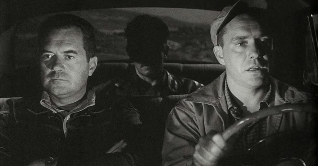 Still from The Hitch-Hiker. A killer sits in the back seat, shrouded in shadow, as his two hostages sit up front, driving him to Mexico.