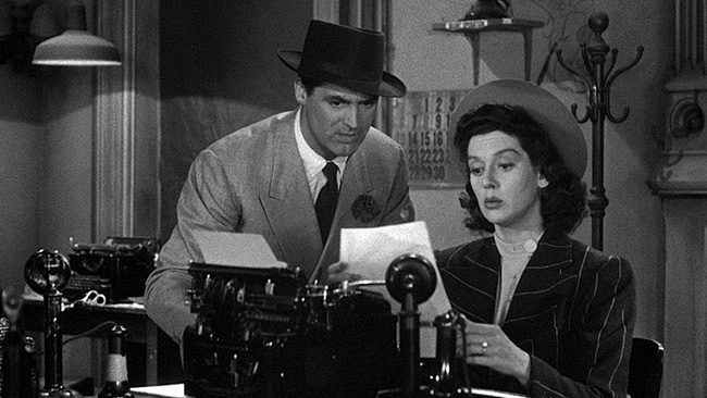 Still from His Girl Friday. Cary Grant reads over Rosalind Russell’s shoulder as she reviews a page from her typewriter.