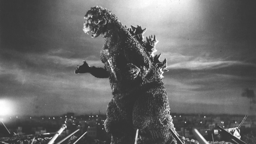 Black and white image of Godzilla towering over a city with ominous clouds in the distance.