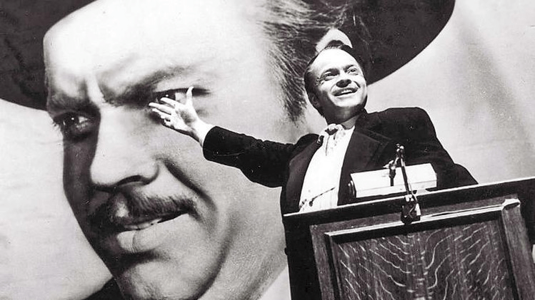 Orson Welles in Citizen Kane, standing at the podium for a campaign rally in front of a giant poster of his own face.