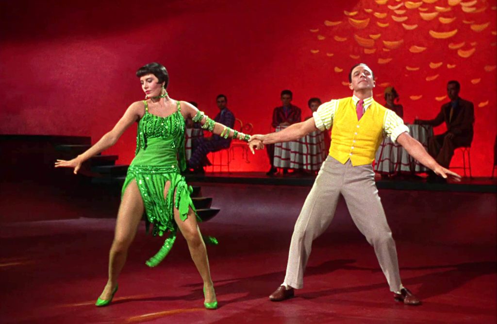 Cyd Charise and Gene Kelly pose, mid-dance in a stylized red dance hall set.