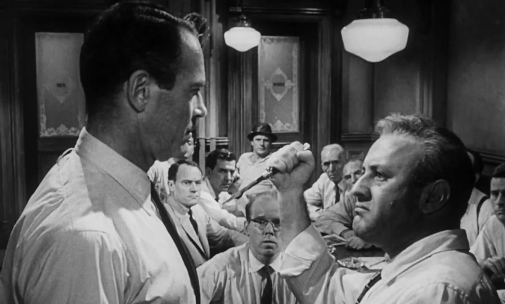 Lee J. Cobb holds a switchblade up to Henry Fonda in front of the other jurors to try and demonstrate how the wounds on the murder victim would have been made.