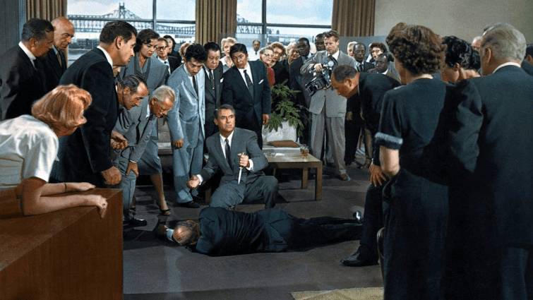 Cary Grant as Roger Thornhill, holding the knife used to murder a UN Ambassador after pulling it out of the ambassador's back. A crowd of people stares at him, convinced he's the killer.
