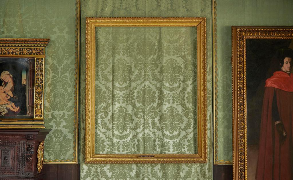 Photograph of the empty frame where Rembrant's Christ in the Storm on the Sea of Galilee once hung in the Dutch Room of the Isabella Stewart Gardner Museum. A wood picture frame with nothing inside, revealing the green patterned wallpaper behind it.